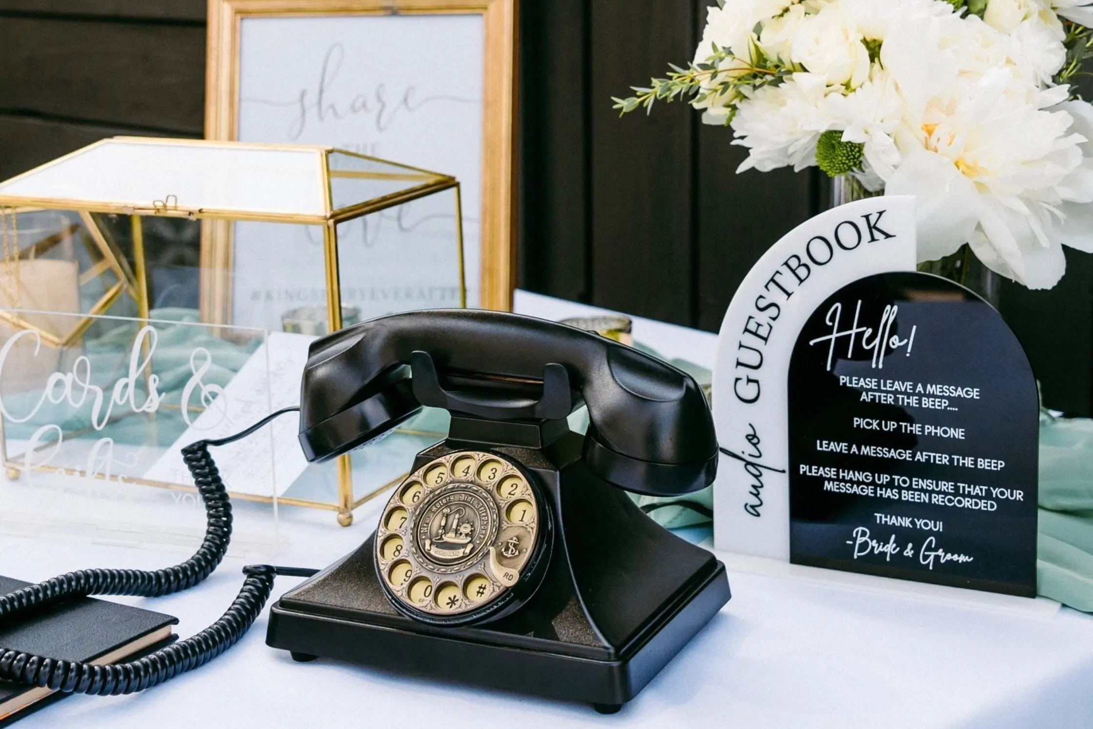Telefon negru cu disc pe o masă, lângă un panou Audio Guestbook și o cutie pentru felicitări