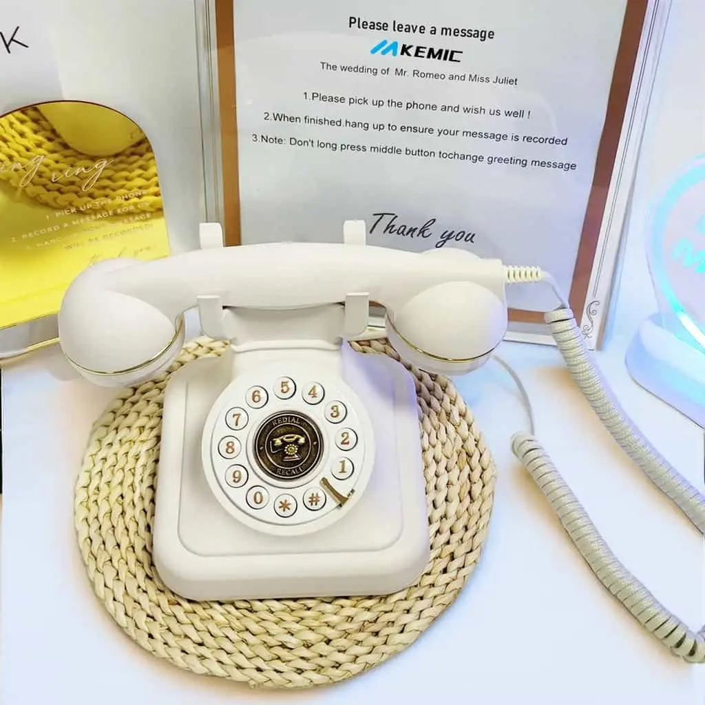 Telefon retro alb Elegance70 White pe un suport împletit, în fața unui panou cu instrucțiuni
